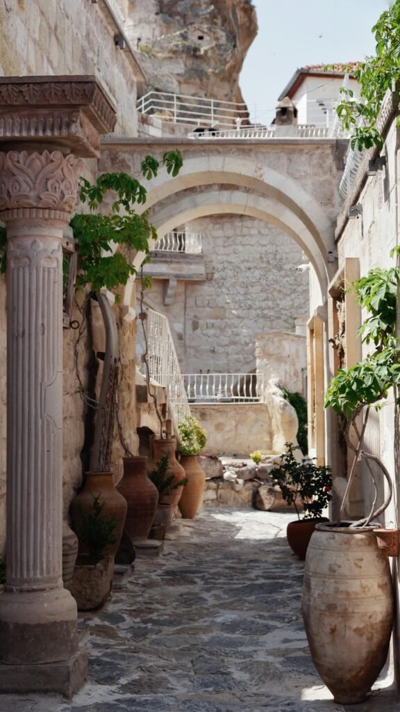 Charming stone alley with arches, pottery, and plants under a sunny sky, evoking a Mediterranean vibe.