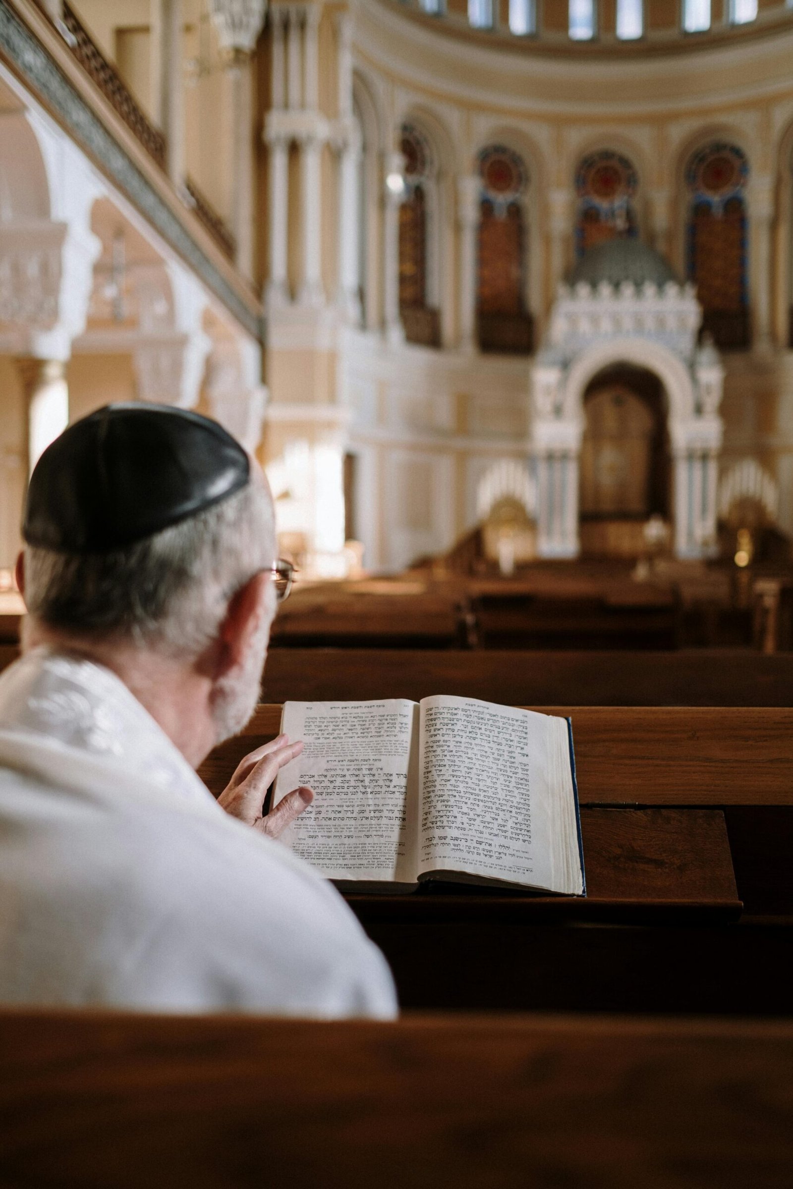 A man wearing a kippah reads religious texts inside a beautifully ornate synagogue.