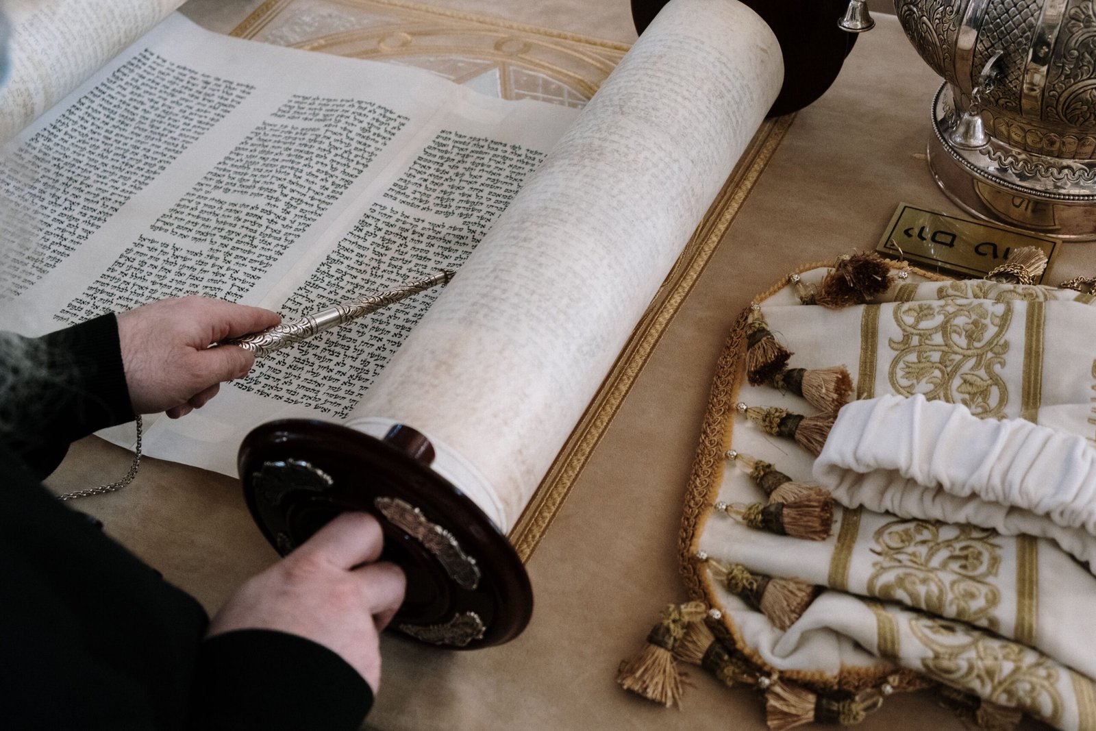 pexels-photo-5986499-5986499 Person reading a Torah scroll using a yad in a traditional synagogue setting.